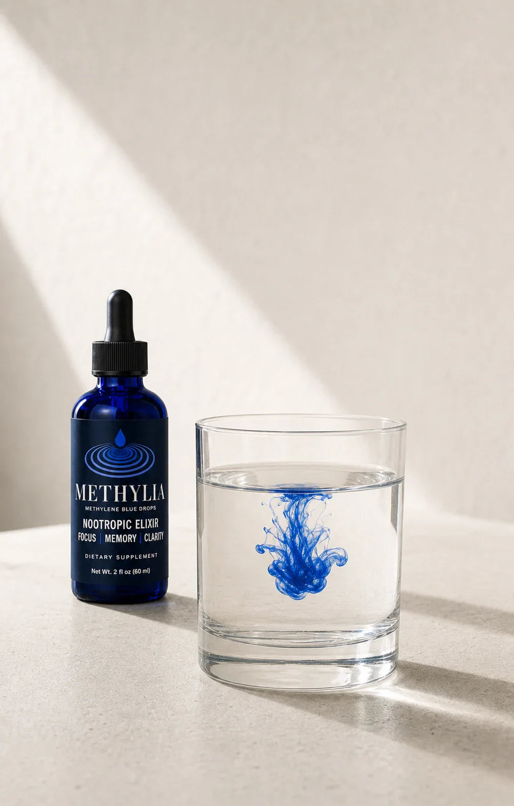Methylia methylene blue drops bottle beside a clear glass of water with a blue bloom.